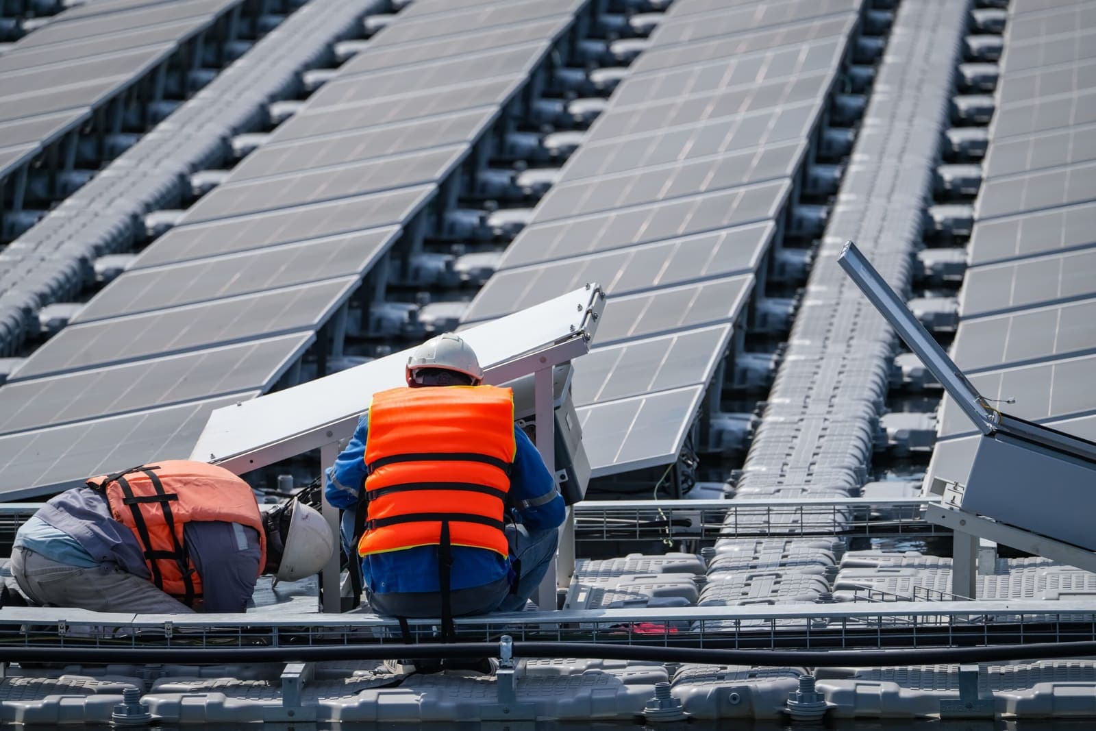 Two installers in orange safety vests fitting panels on a large commercial roof