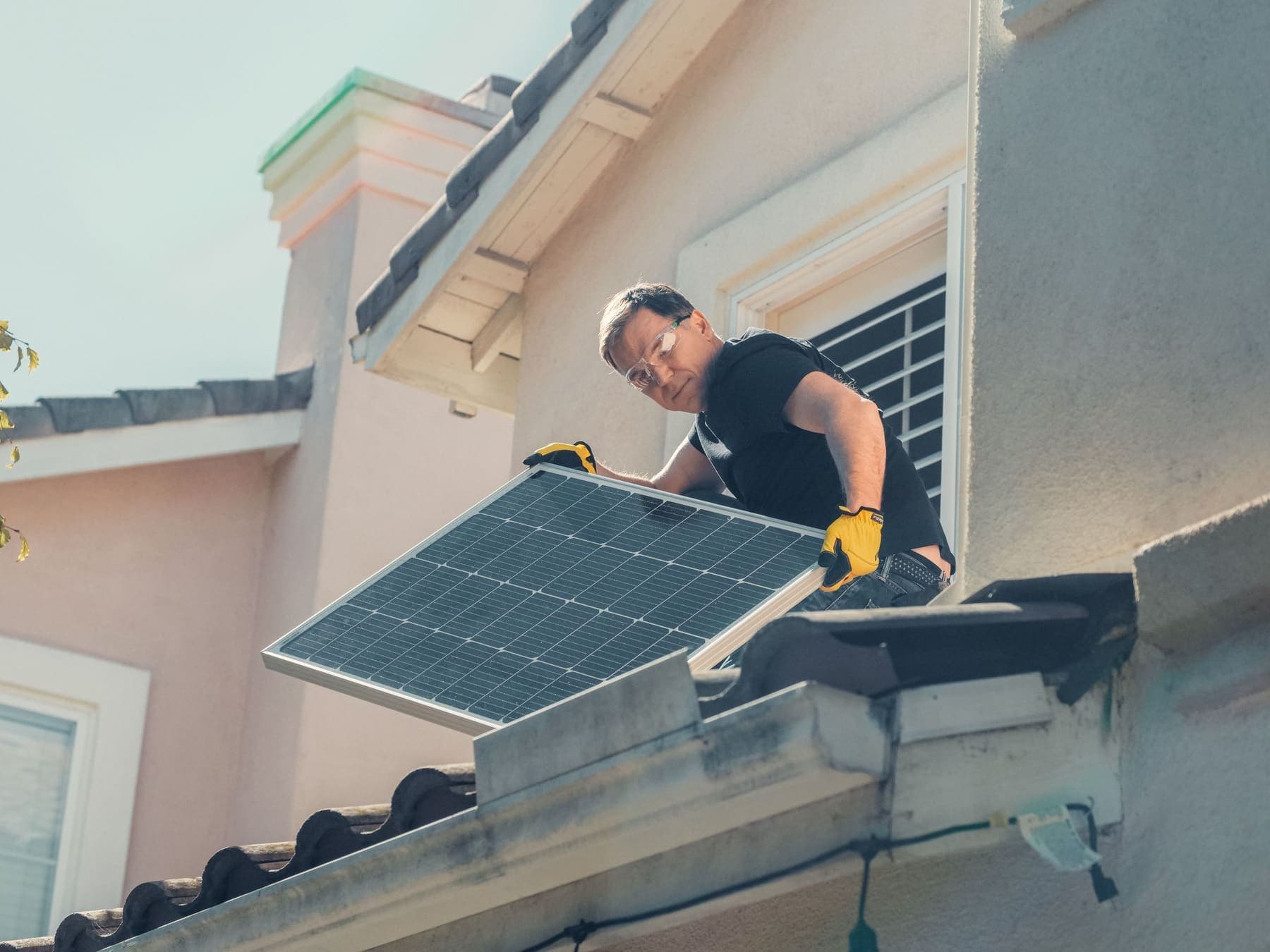 An installer in safety glasses and gloves lifting a solar panel onto a roof