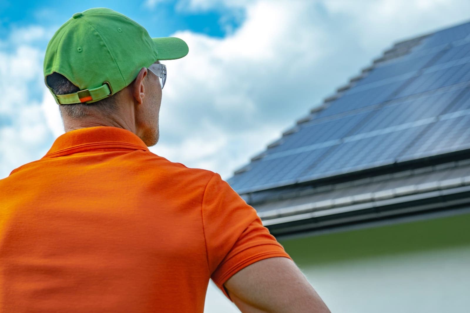 A technician in a green cap and orange shirt inspecting rooftop panels